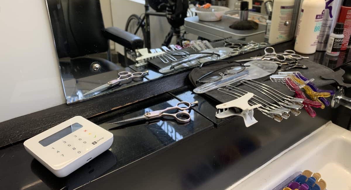 A SumUp card reader on a hair salon counter beside scissors and clips