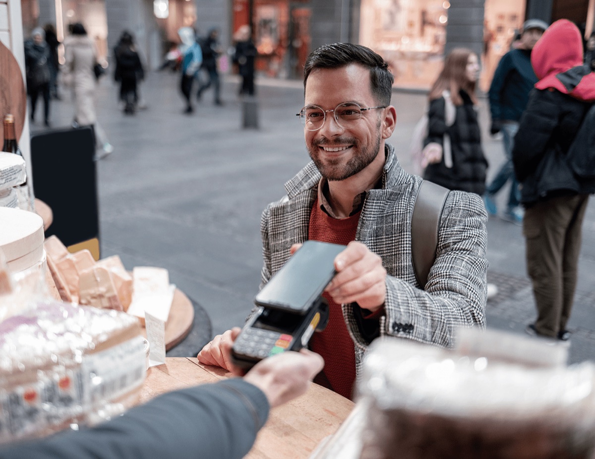 A smiling customer paying by contactless card on a handheld terminal at an outdoor market stall